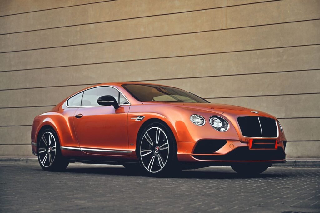 Elegant orange Bentley car parked in front of a modern architectural wall, showcasing luxury and style.