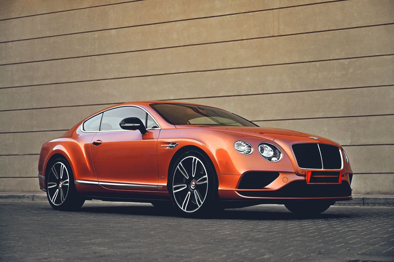 Elegant orange Bentley car parked in front of a modern architectural wall, showcasing luxury and style.
